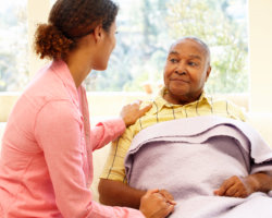 caregiver holding the hands of patient lying in the bed